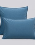 Duas almofadas com fronhas Stone azuis em percale 100% algodão sobre fundo cinzento.