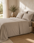 Lençol de cima Stone bege integrado numa cama com almofadas coordenadas, num quarto iluminado por luz natural.