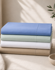 Lençóis de Cima Royal em percale dobrados nas cores azul, verde, branco e caqui