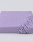 Lençol ajustável Stone lavanda dobrado, com o elástico visível sobre fundo cinzento.