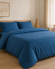 Capa de edredão Charming em flanela chambray cor Azul sobre cama arrumada em quarto de madeira clara com luz natural — BellaGoma
