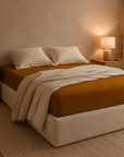 Fronhas Charming ocre em flanela chambray numa cama com roupa branca e candeeiro aceso, num ambiente acolhedor - BellaGoma