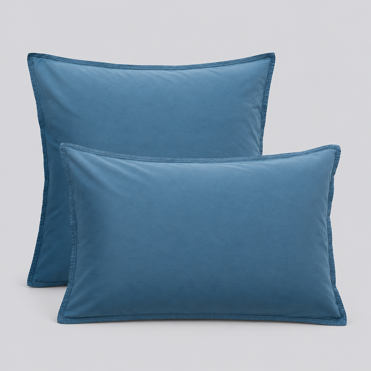 Duas almofadas com fronhas Stone azuis em percale 100% algodão sobre fundo cinzento.