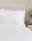 Fronhas BellaLux brancas sobre cama elegante em tons neutros