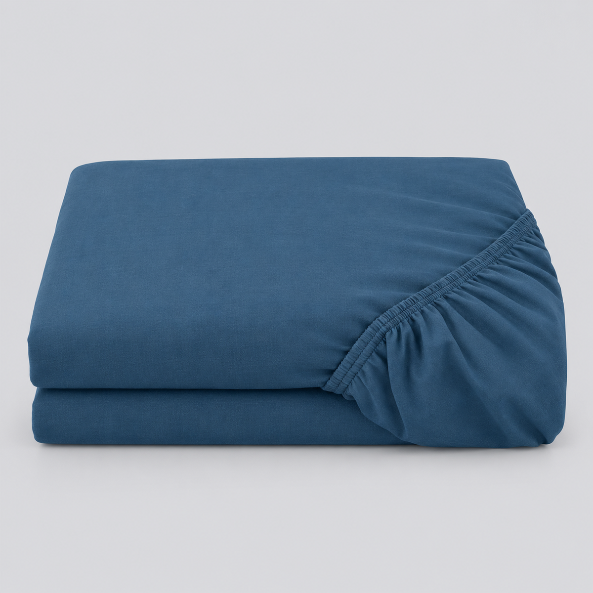 Lençol ajustável Stone azul dobrado, com o elástico visível sobre fundo cinzento.