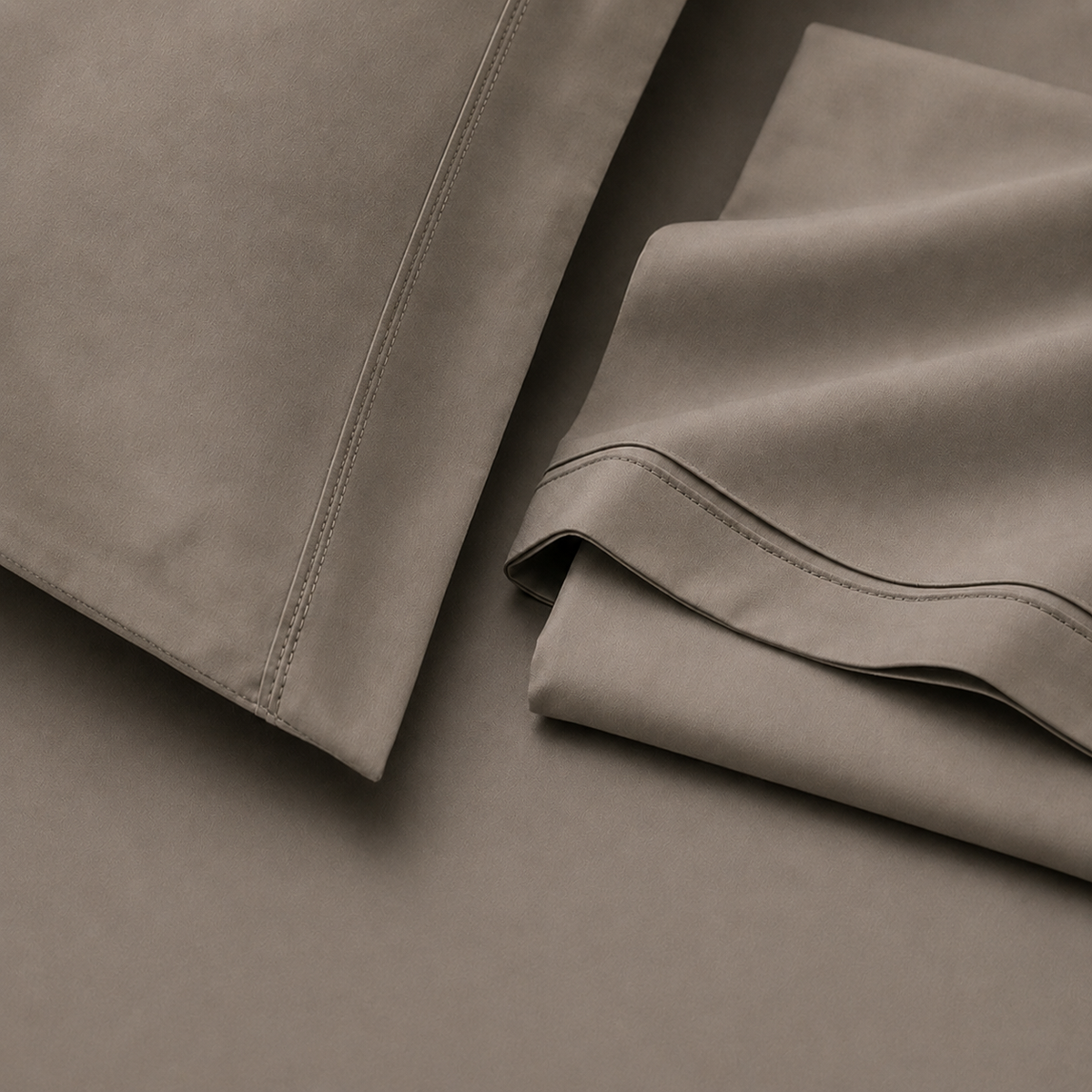 Pormenor do tecido e das bainhas da roupa de cama Stone em tons neutros.