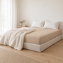 Lençol Ajustável Charming em Areia numa cama com sommier forrado, num quarto luminoso.
