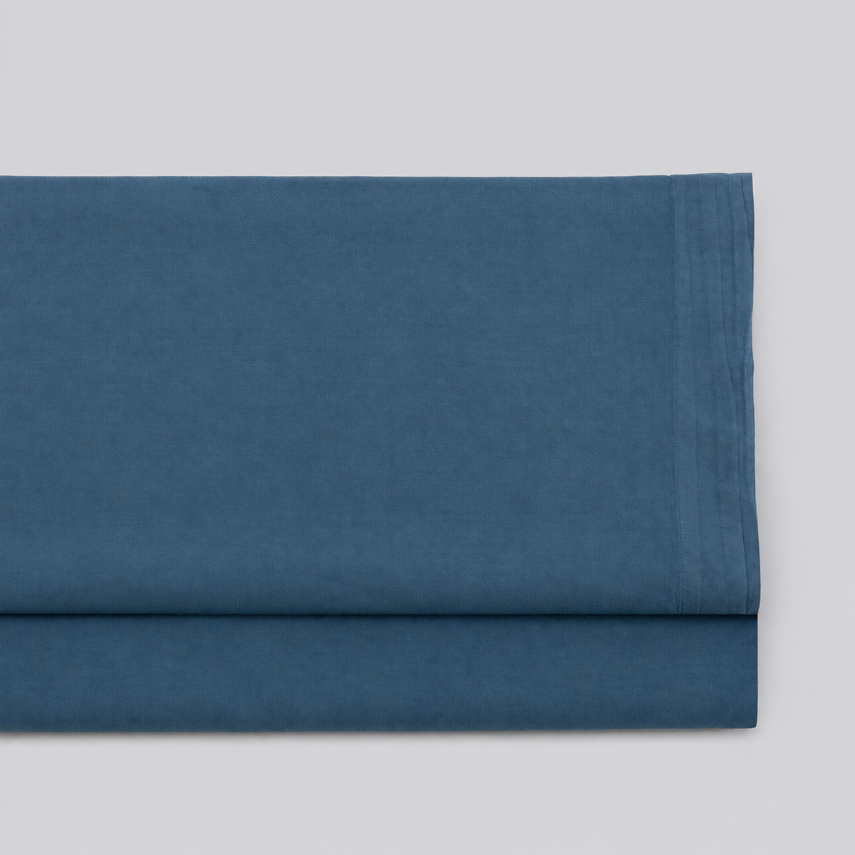 Lençol de cima Stone azul em percale 100% algodão, dobrado com a bainha superior visível.