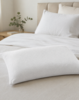 Almofada de flocos de viscoelástico sobre cama com roupa de cama em tons bege e cabeceira em madeira natural