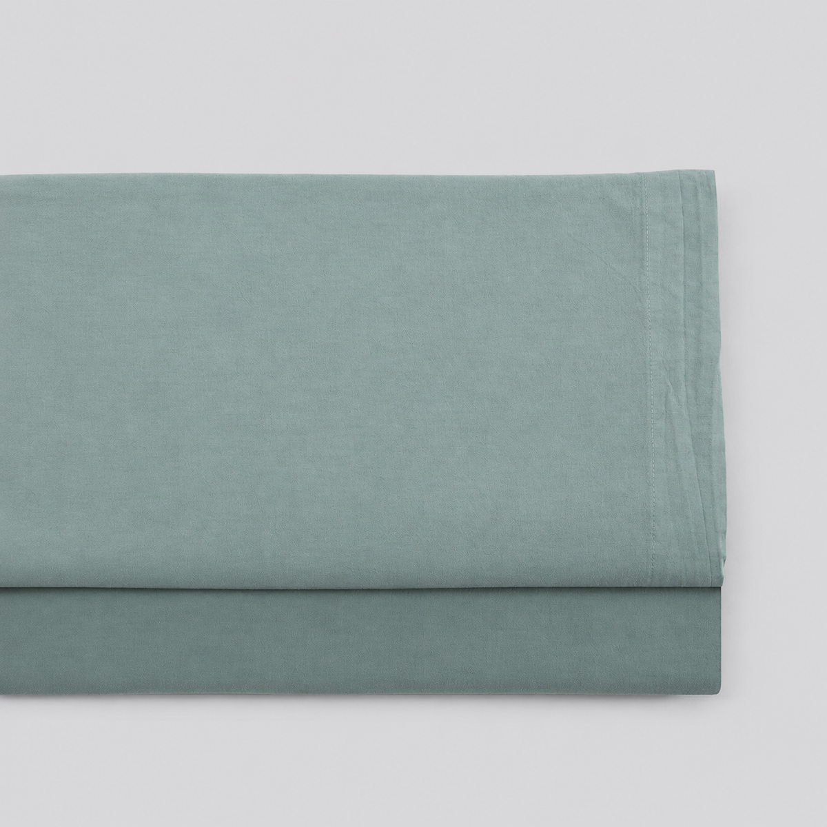 Lençol de cima Stone verde em percale 100% algodão, dobrado com a bainha superior visível.